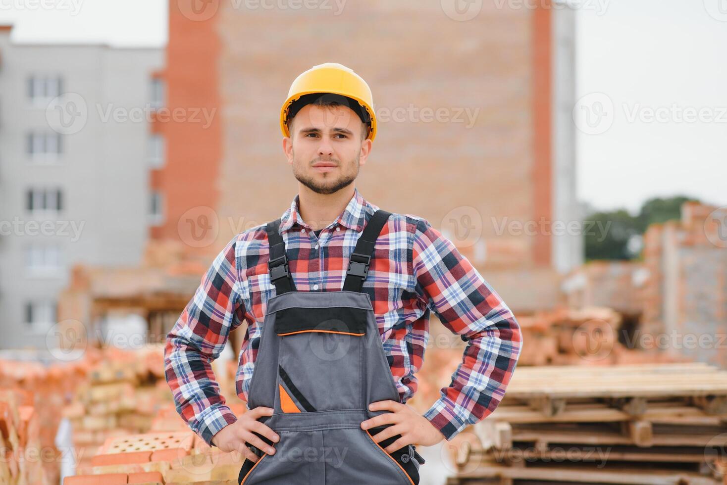 Construction worker man in work clothes and a construction helmet. Portrait of positive male builder in hardhat working at construction site. photo