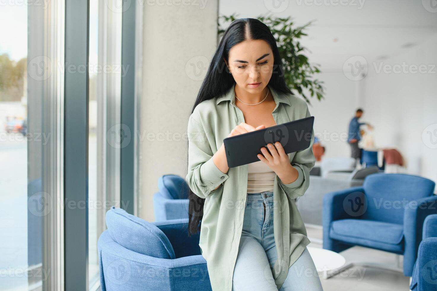 Young modern female freelancer in airport lounge or business center and works using digital tablet, creating new design project photo