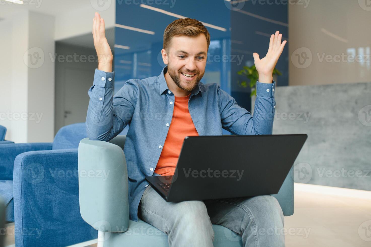 happy smiling remote online working man in casual outfit with laptop in joyful successful winning gesture sitting in an coworking office at a work desk. photo