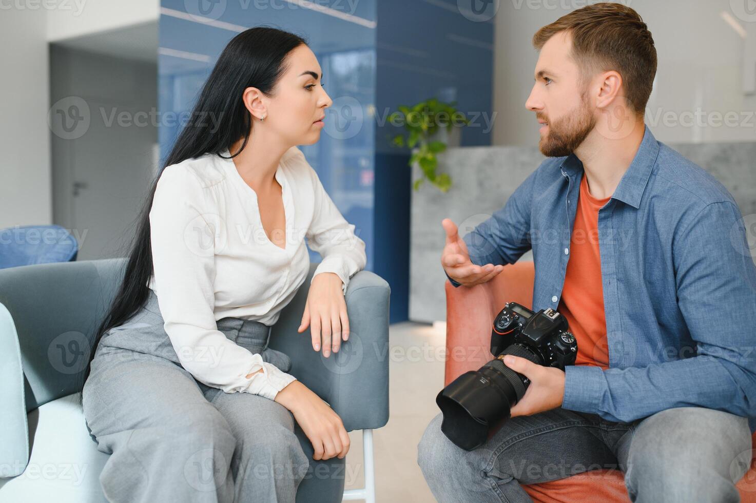Photographer in office shows photo model in camera. Consultant adjusts activities company as whole. Photo session employees in workplace. Manager well-executed project. Photos best employees company.