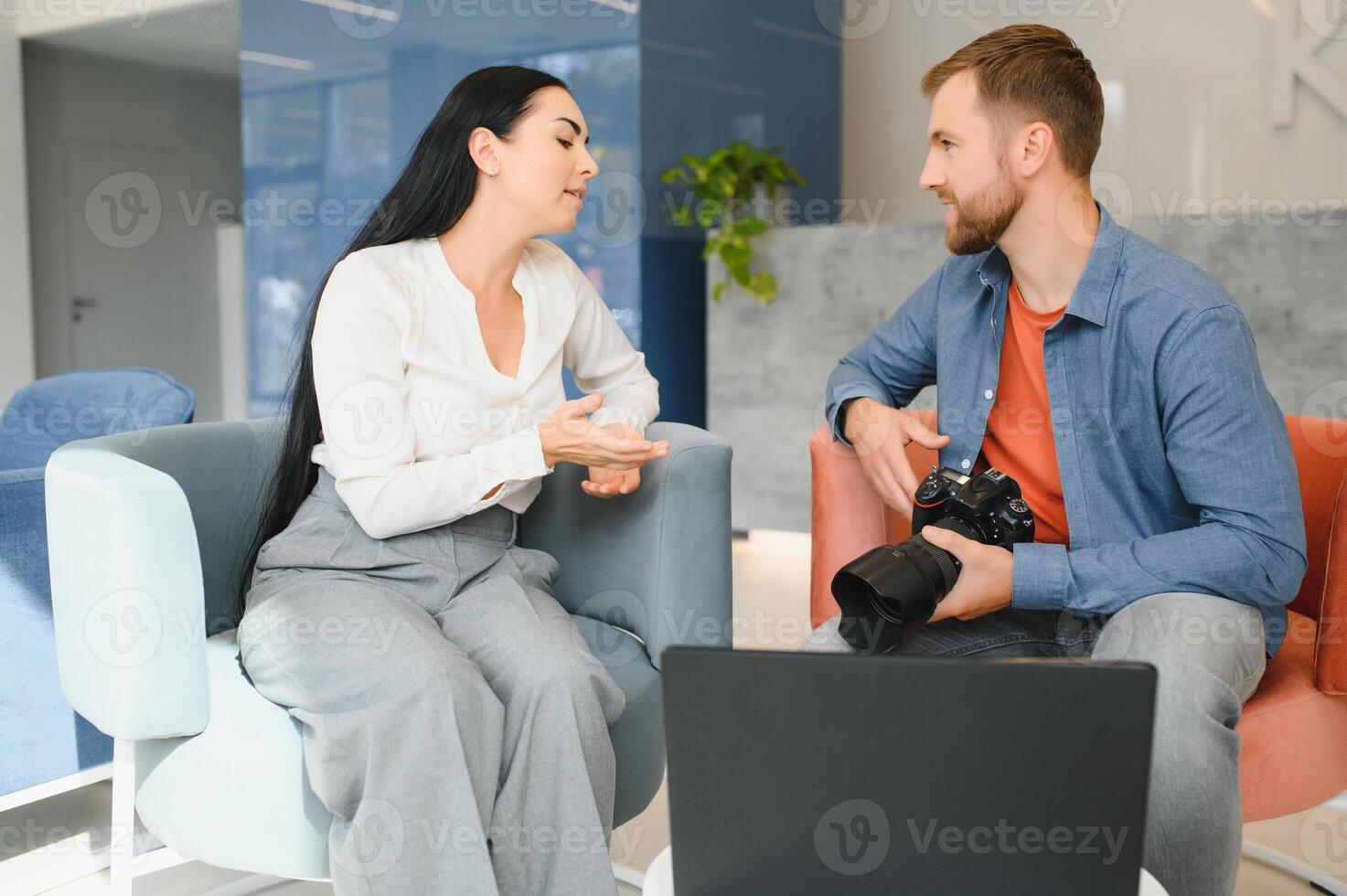 Photographer in office shows photo model in camera. Consultant adjusts activities company as whole. Photo session employees in workplace. Manager well-executed project. Photos best employees company.