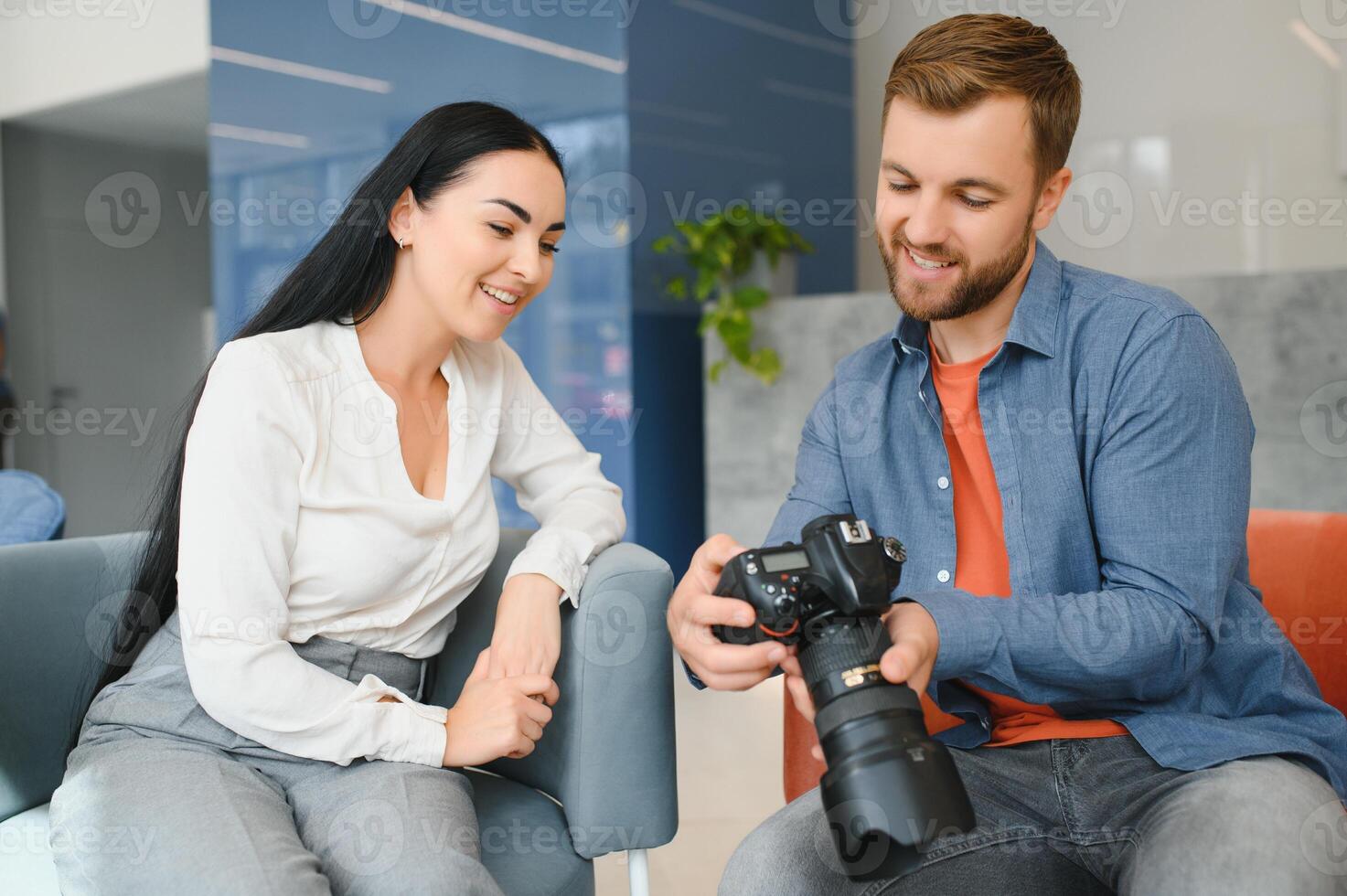 Young photographer man in blue shirt watching photo with client woman after photo session and smiling and looking at each other