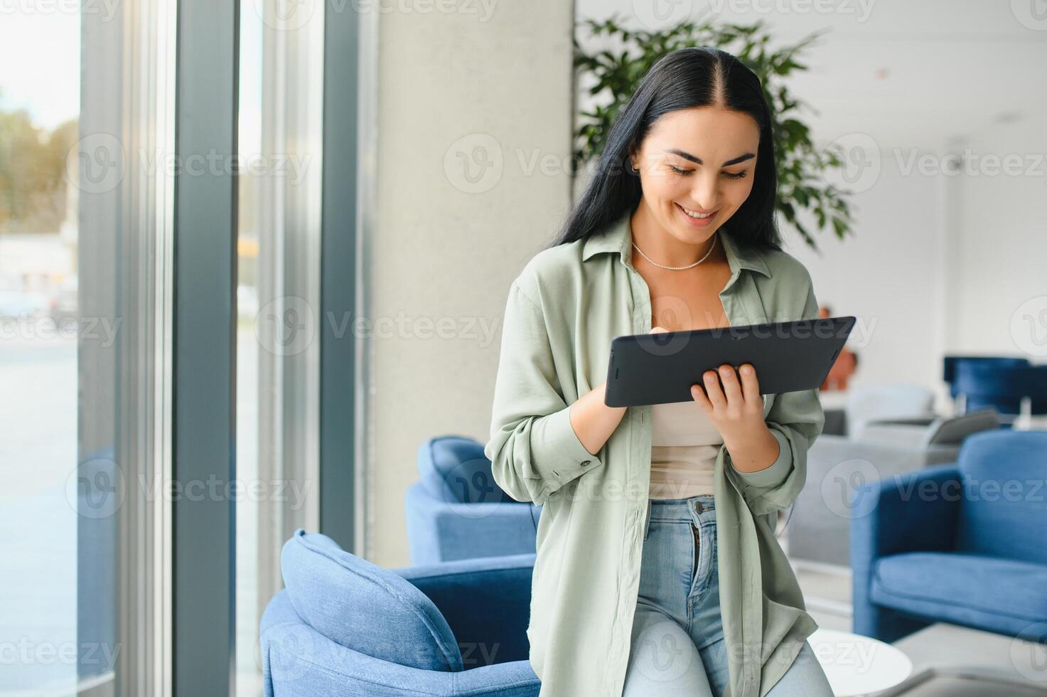 Young modern female freelancer in airport lounge or business center and works using digital tablet, creating new design project photo