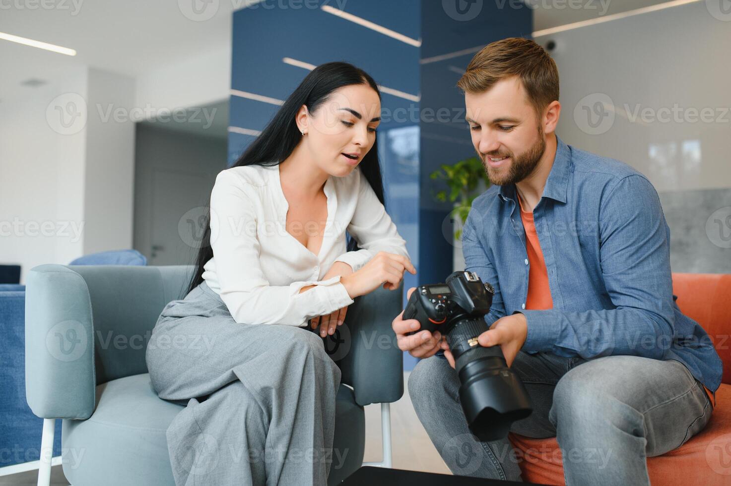 Photographer in office shows photo model in camera. Consultant adjusts activities company as whole. Photo session employees in workplace. Manager well-executed project. Photos best employees company.