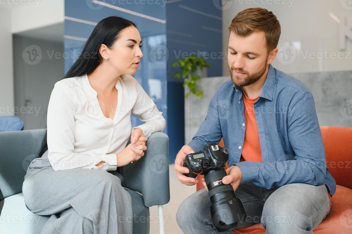 Photographer in office shows photo model in camera. Consultant adjusts activities company as whole. Photo session employees in workplace. Manager well-executed project. Photos best employees company.