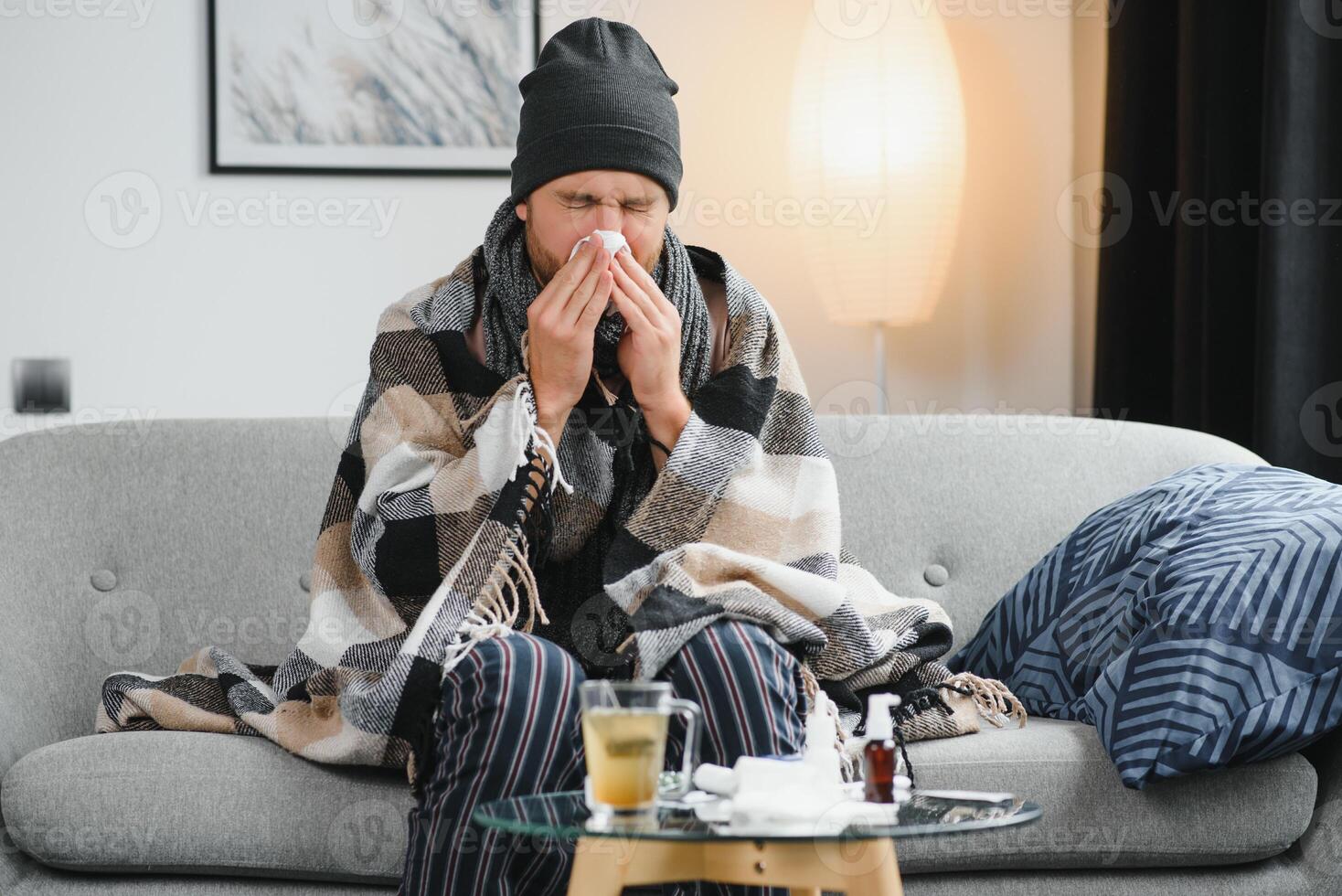 Sick man on sofa at home and blowing nose photo
