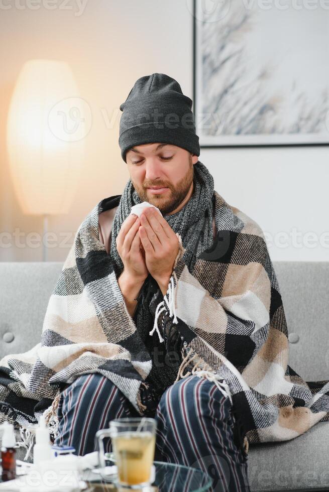 Sick man on sofa at home and blowing nose photo