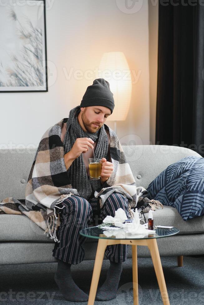 A sick man sits at home on a gray sofa with a blanket. Illness, protection, coronavirus, illness, flu photo
