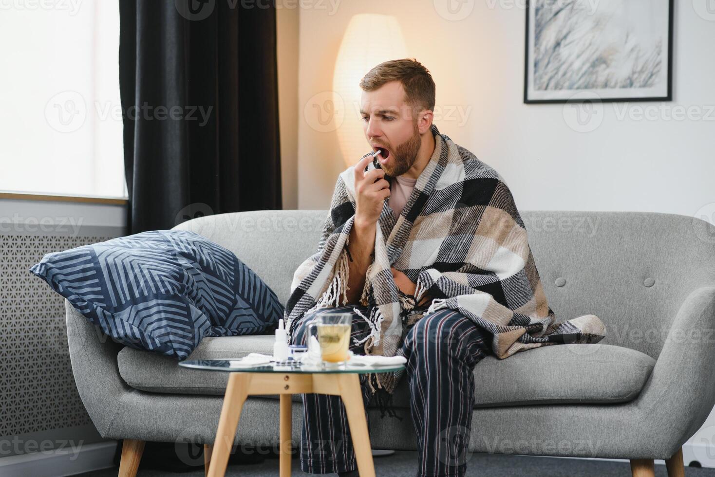 rhinitis, medicine and healthcare concept - sick man in blanket using oral spray at home photo