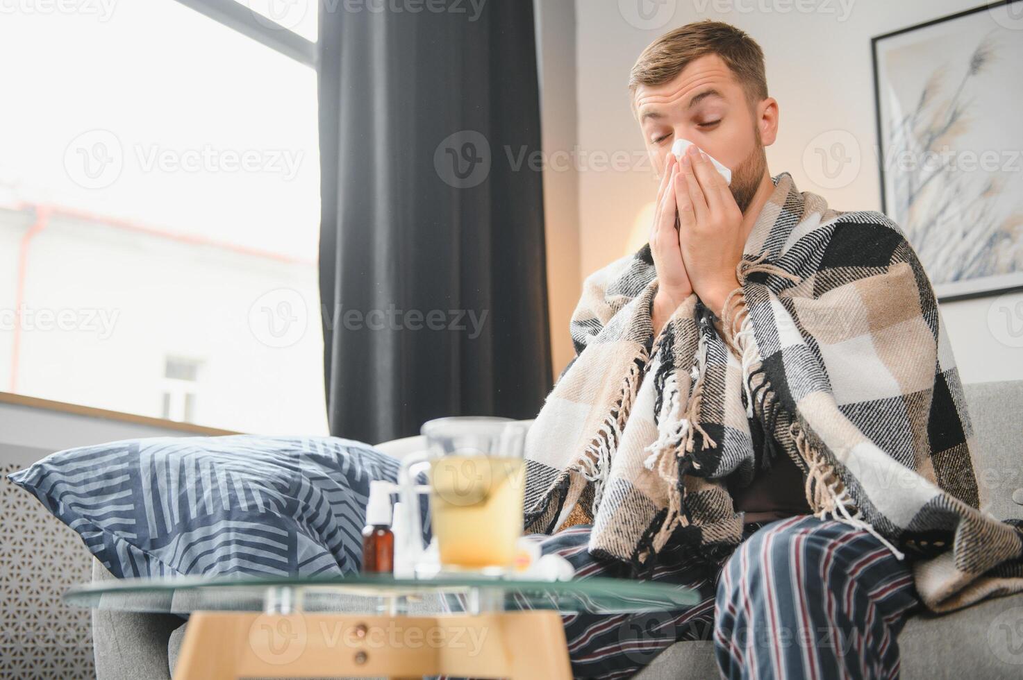 Sick man on sofa at home and blowing nose photo