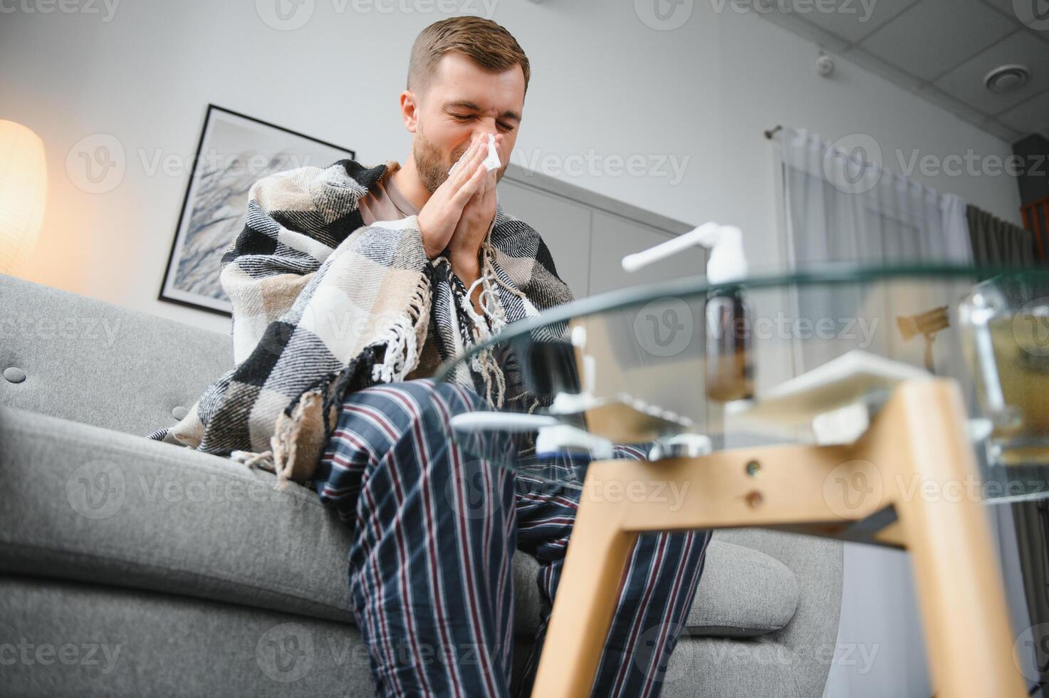 Sick man on sofa at home and blowing nose photo