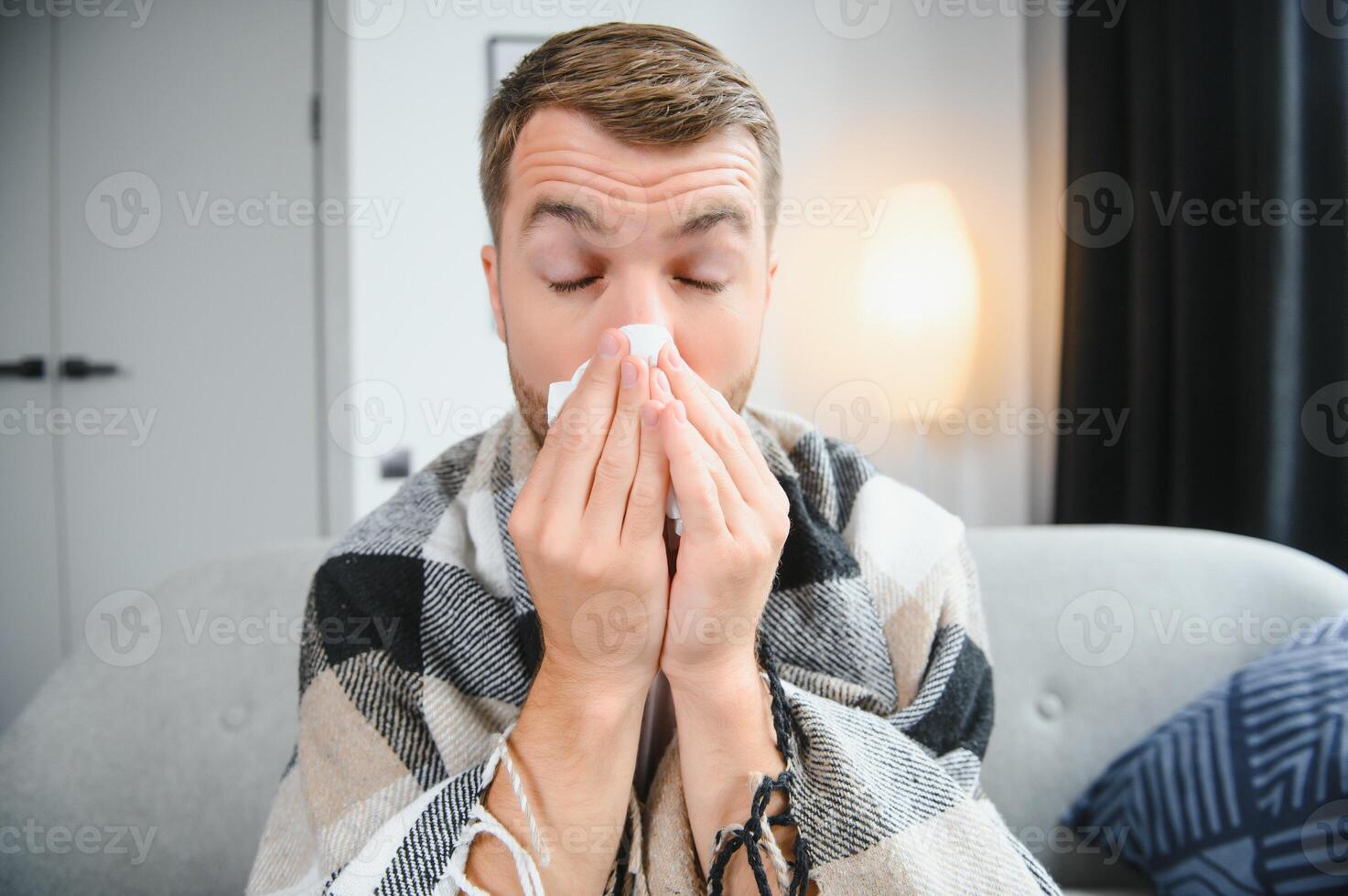 Sick man on sofa at home and blowing nose photo