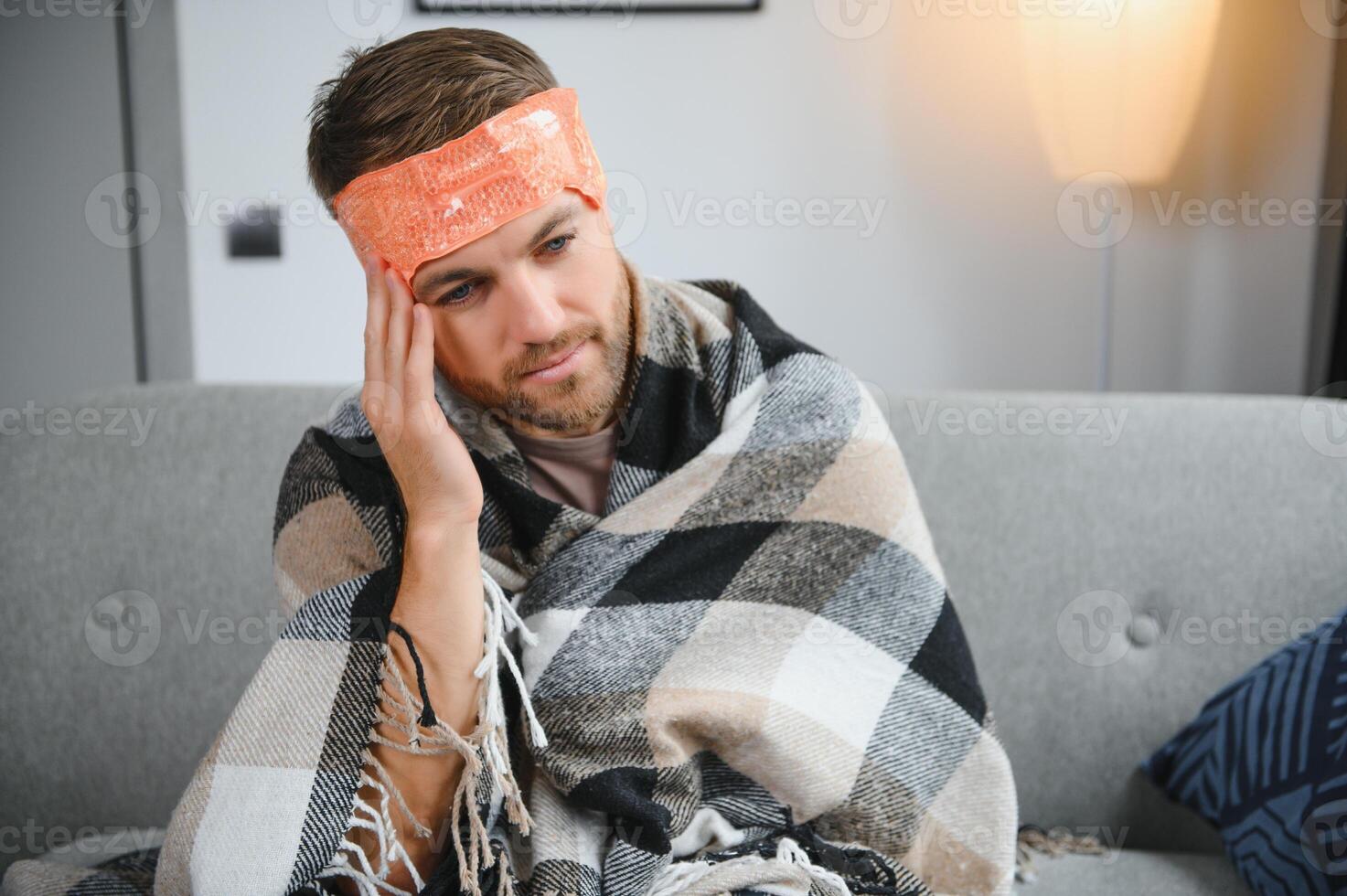 Young man suffering from cold at his home. Shot of a young man sitting on his bed while feeling unwell at home. Trying to stay warm. Sick man photo