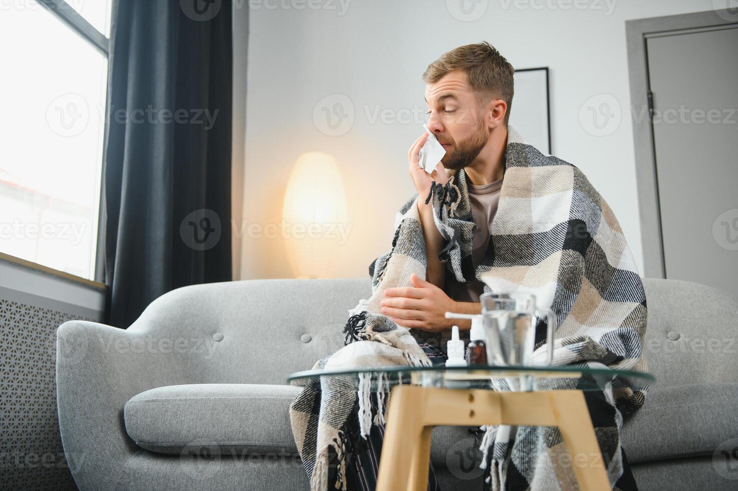 Sick man on sofa at home and blowing nose photo