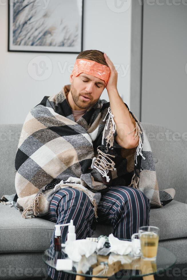A sick man sits at home on a gray sofa with a blanket. Illness, protection, coronavirus, illness, flu photo