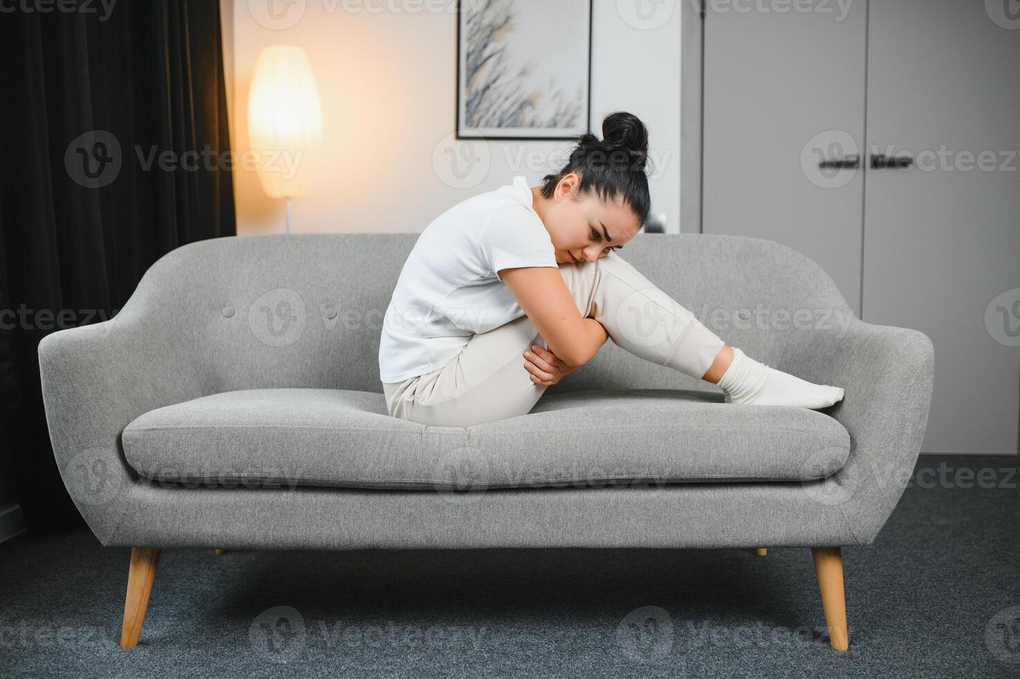 Portrait of beautiful young woman with depressed facial expression sitting on grey textile couch. Cyber bullying victim concept. Sad female in her room. Background, copy space photo