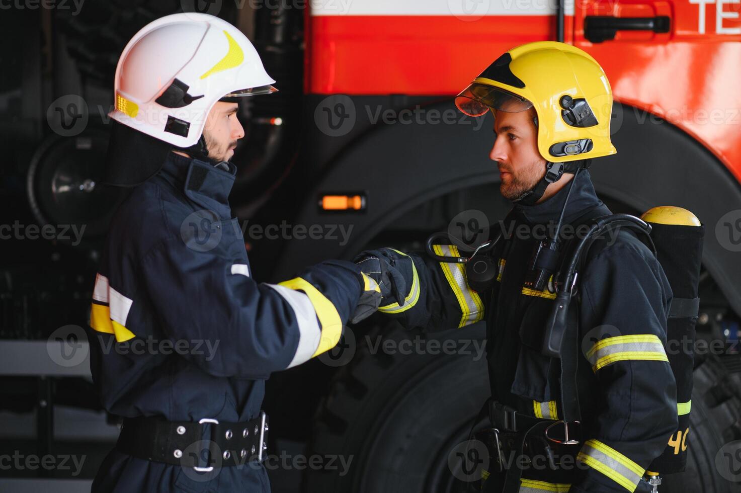 Two firefighters in protective clothing in helmets with fire engine, friendly handshake photo