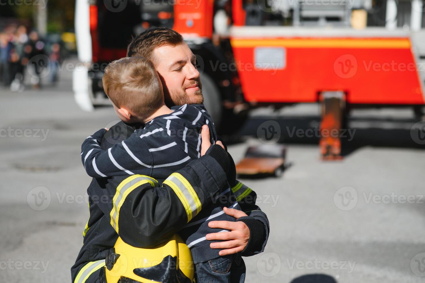 Dirty firefighter in uniform holding little saved boy standing on black background. photo