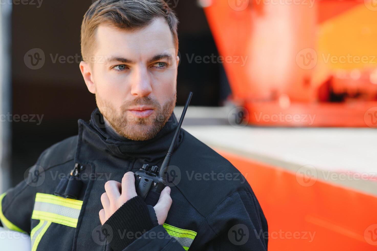 Confident fireman wearing protective uniform standing next to a fire engine in a garage of a fire department photo