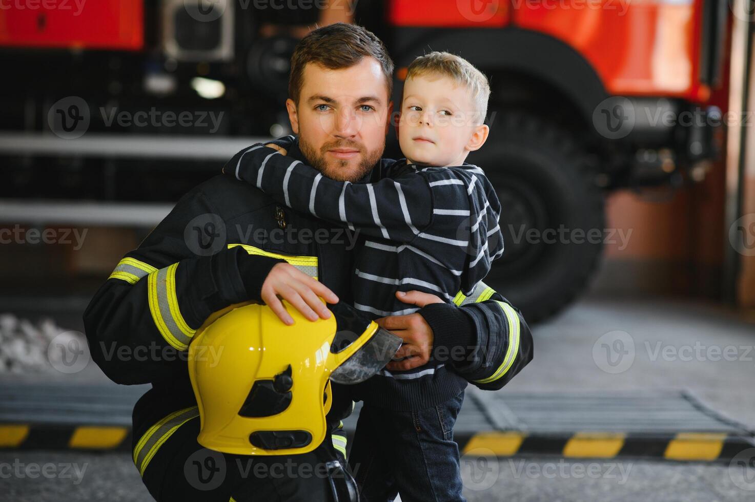 Dirty firefighter in uniform holding little saved boy standing on black background. photo