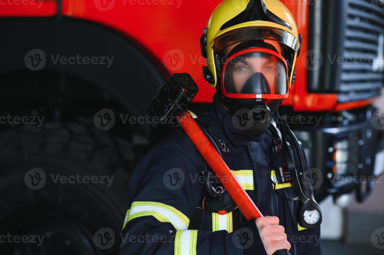 Photo of young fireman with sledgehammer in hands near fire engine