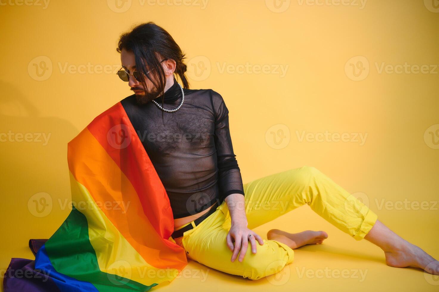gay man with a gay pride flag smiling and looking away on yellow background photo