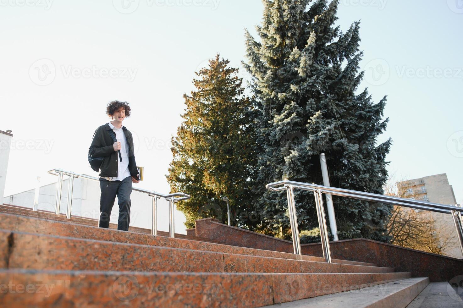 Happy handsome university, college student or young smart successful guy, school pupil with books textbooks smiling outdoors at sunset. Copy space photo