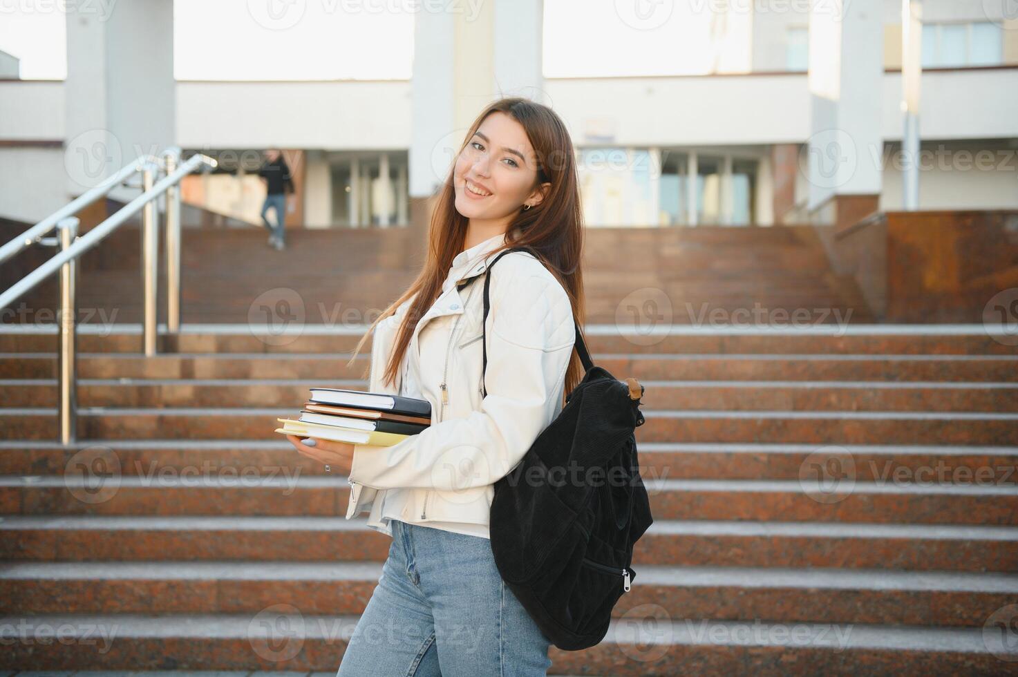 Cheerful attractive young woman with backpack and notebooks standing and smiling. photo