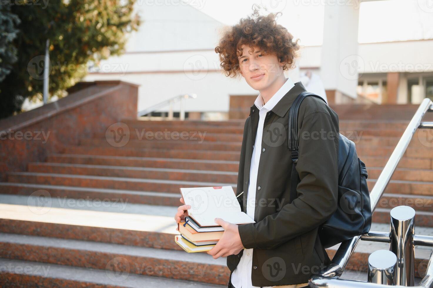 University.Smiling young student man holding a book and a bag on a university background .Young smiling student outdoors Life style.City.Student. photo