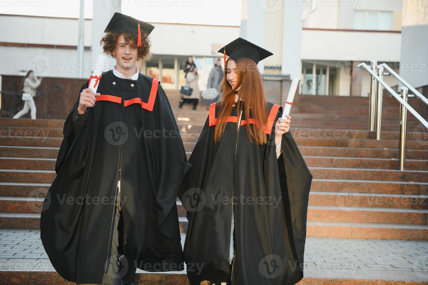Graduates in mantles with diplomas in hands are standing near university. photo