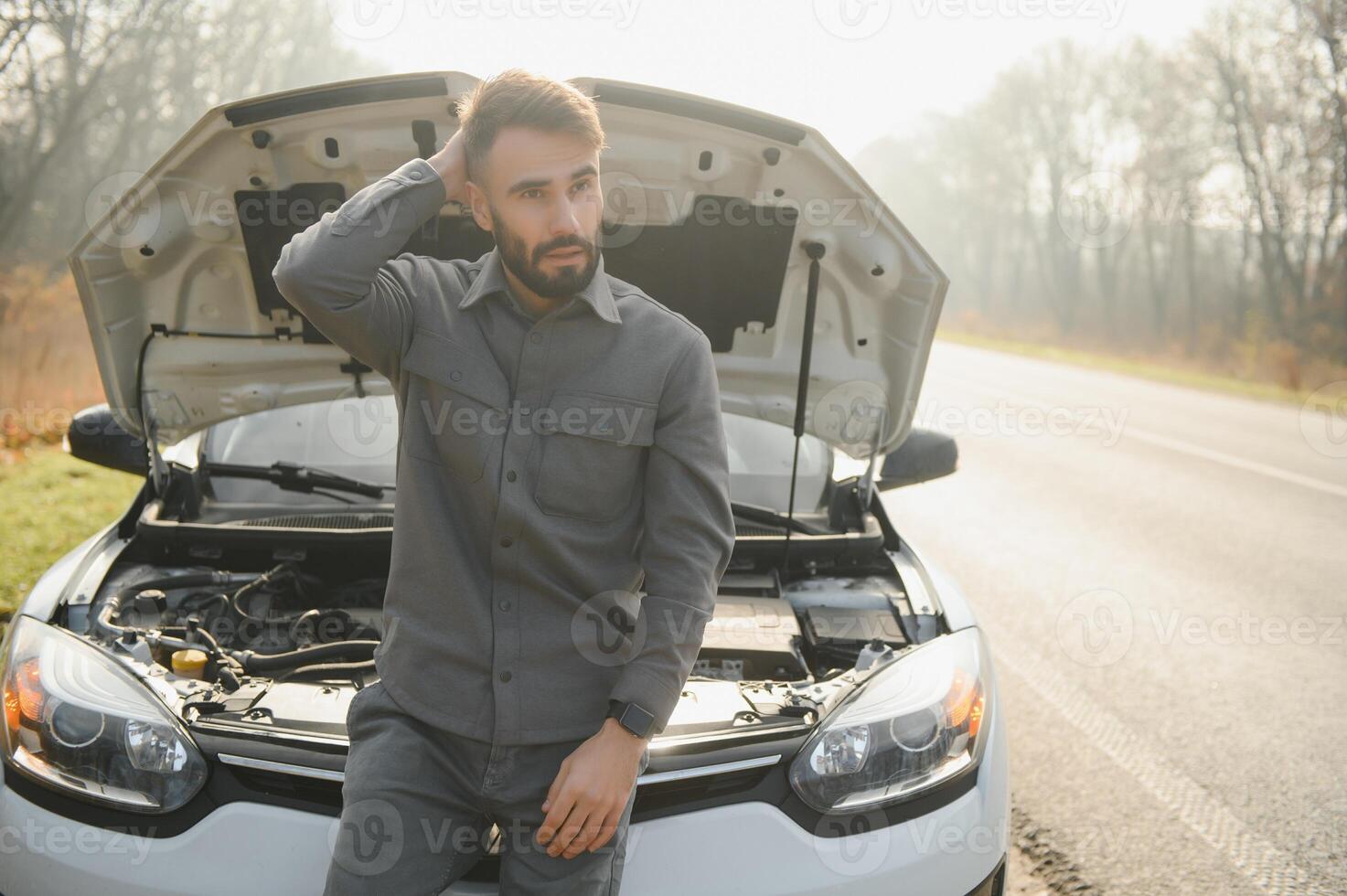 Sad driver holding his head having engine problem standing near broken car on the road. Car breakdown concept photo