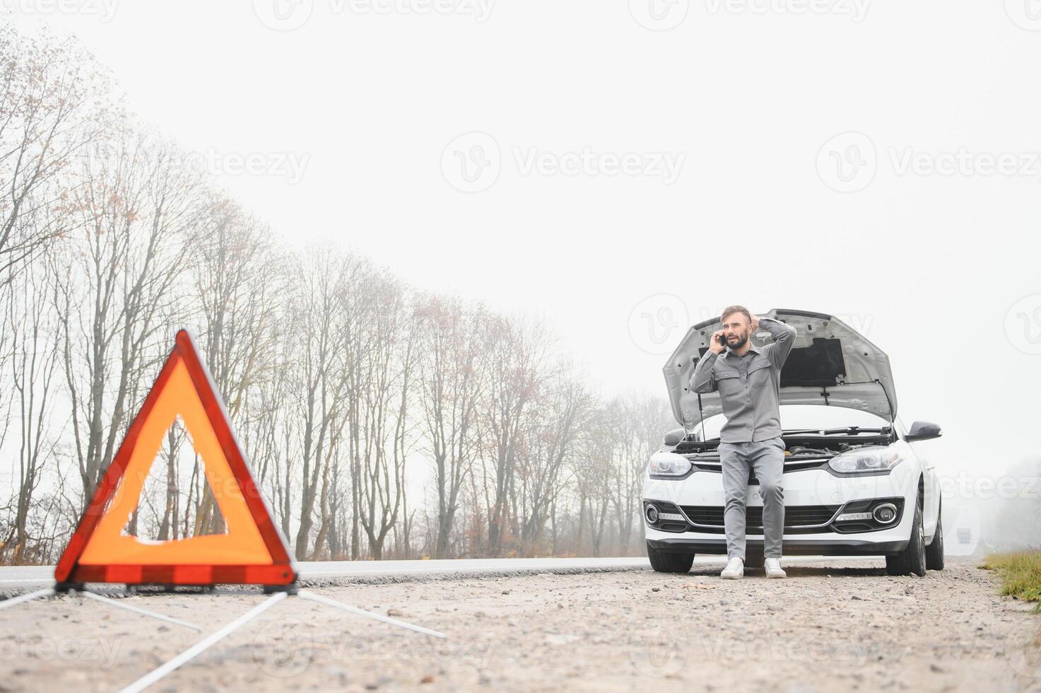 Man use a cellphone call garage in front of the open hood of a broken car on the road in the forest. Car breakdown concept. photo
