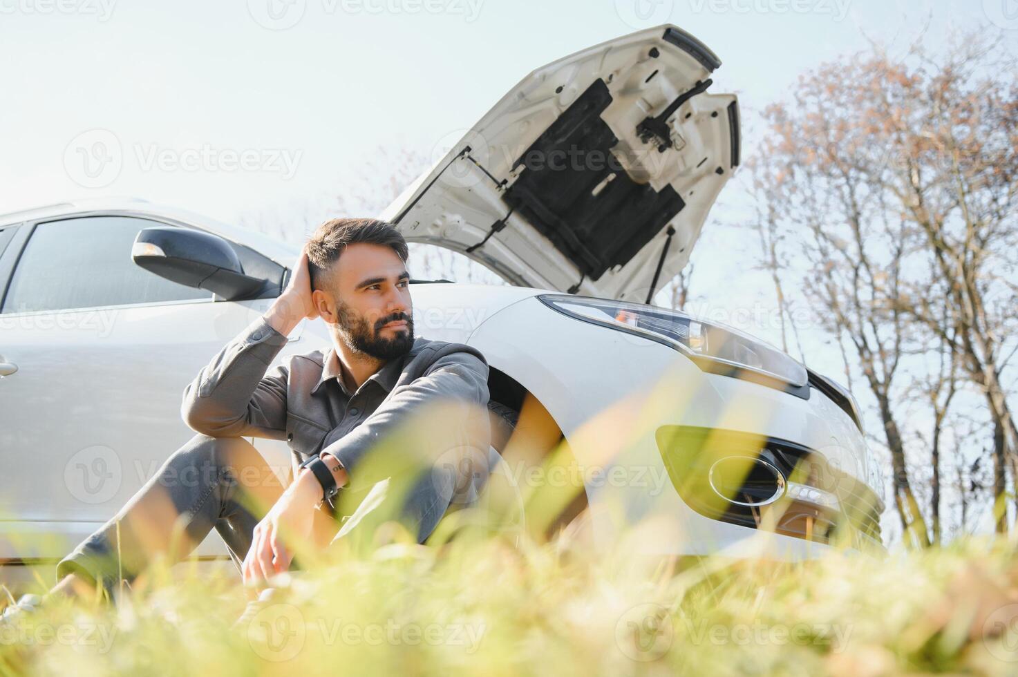 Sad driver holding his head having engine problem standing near broken car on the road. Car breakdown concept photo