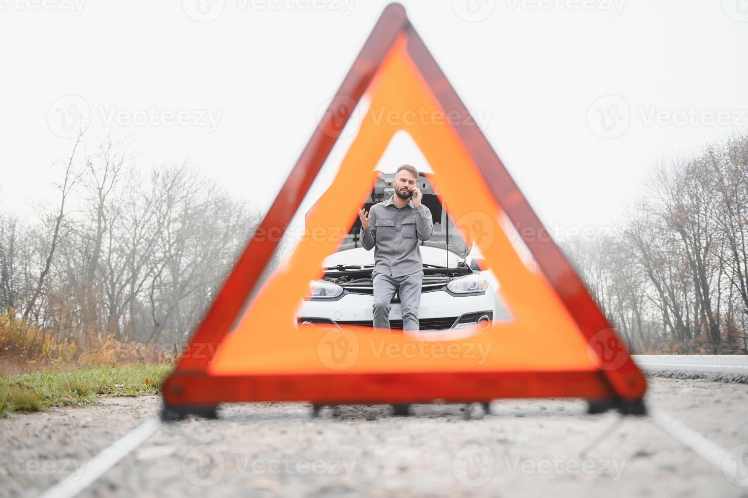 A young man near a broken car with an open hood on the roadside. photo