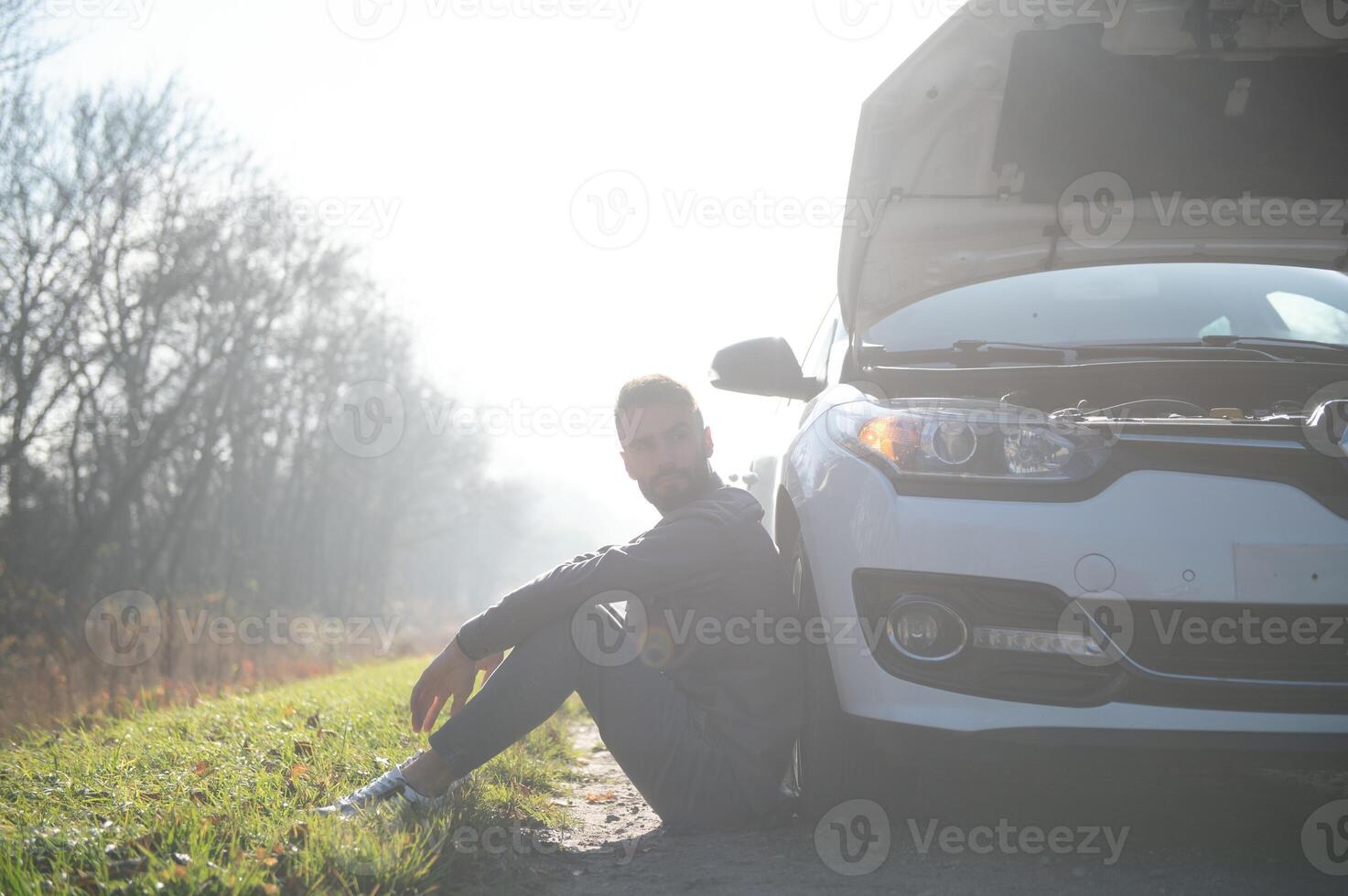 Sad driver holding his head having engine problem standing near broken car on the road. Car breakdown concept photo