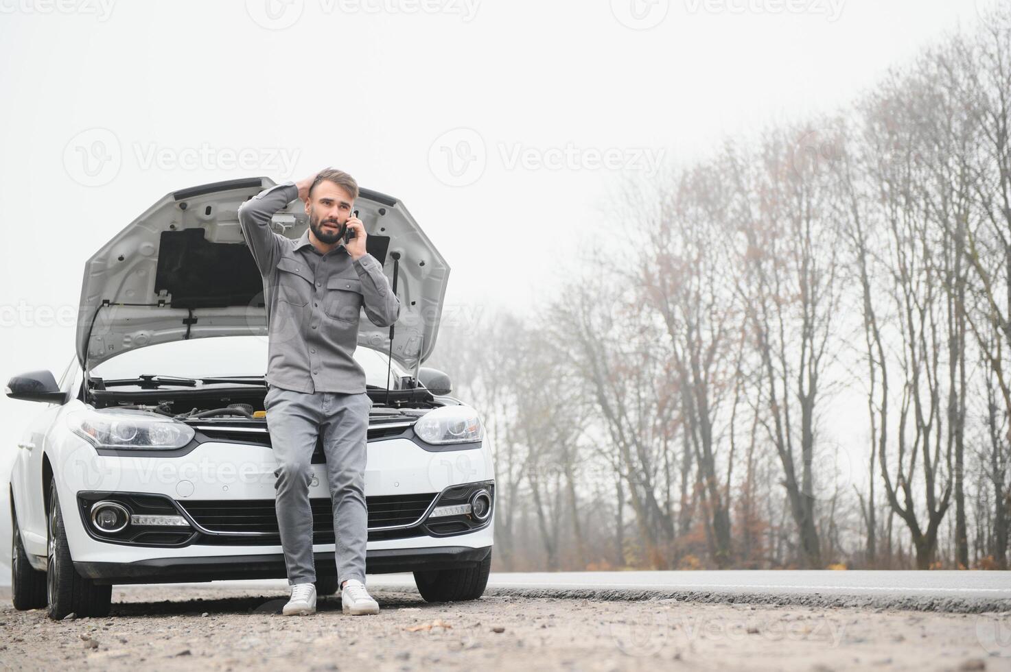 Sad driver calling car service, opening hood, having engine problem standing near broken car on the road. Car breakdown concept photo