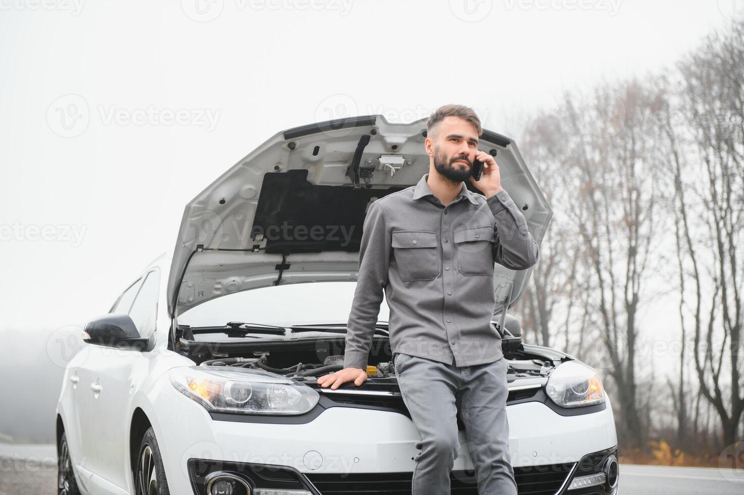 Sad driver calling car service, opening hood, having engine problem standing near broken car on the road. Car breakdown concept photo