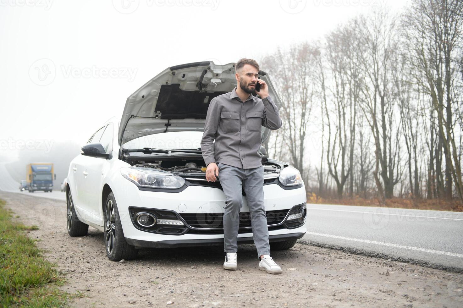 Man use a cellphone call garage in front of the open hood of a broken car on the road in the forest. Car breakdown concept. photo