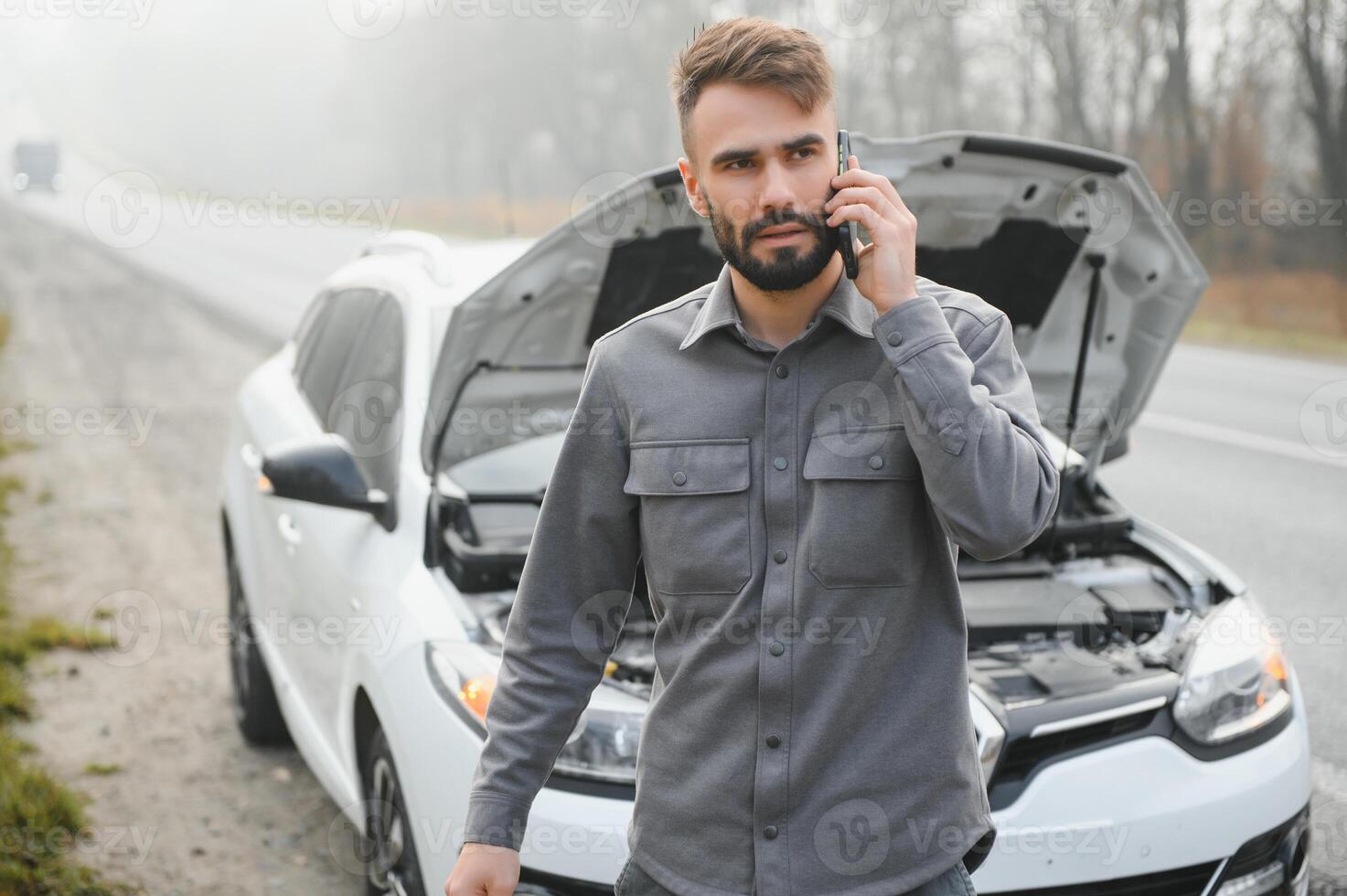 Sad driver calling car service, opening hood, having engine problem standing near broken car on the road. Car breakdown concept photo
