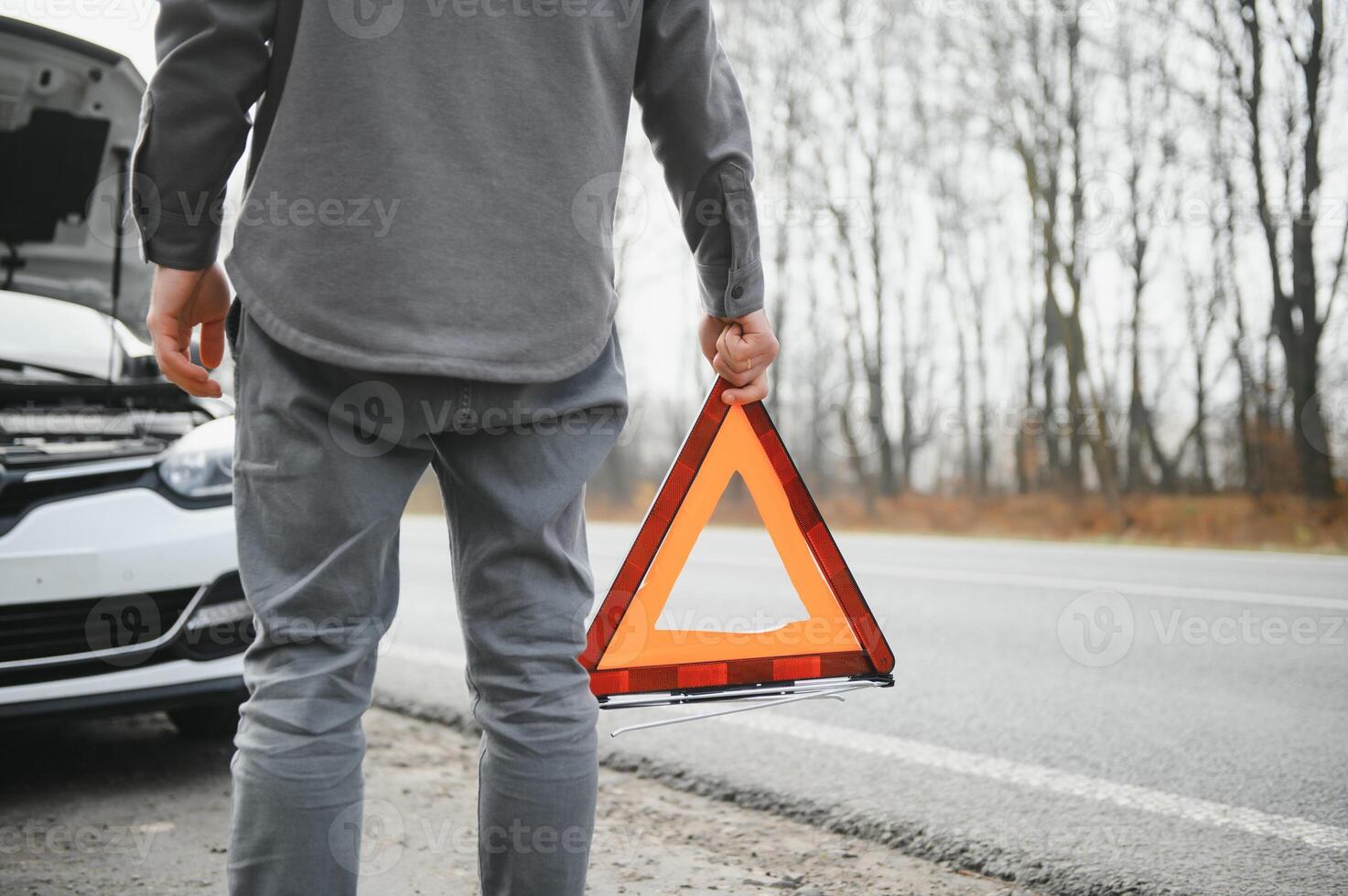A young man near a broken car with an open hood on the roadside. photo