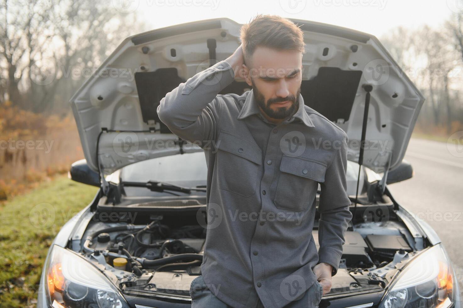 Sad driver calling car service, opening hood, having engine problem standing near broken car on the road. Car breakdown concept photo