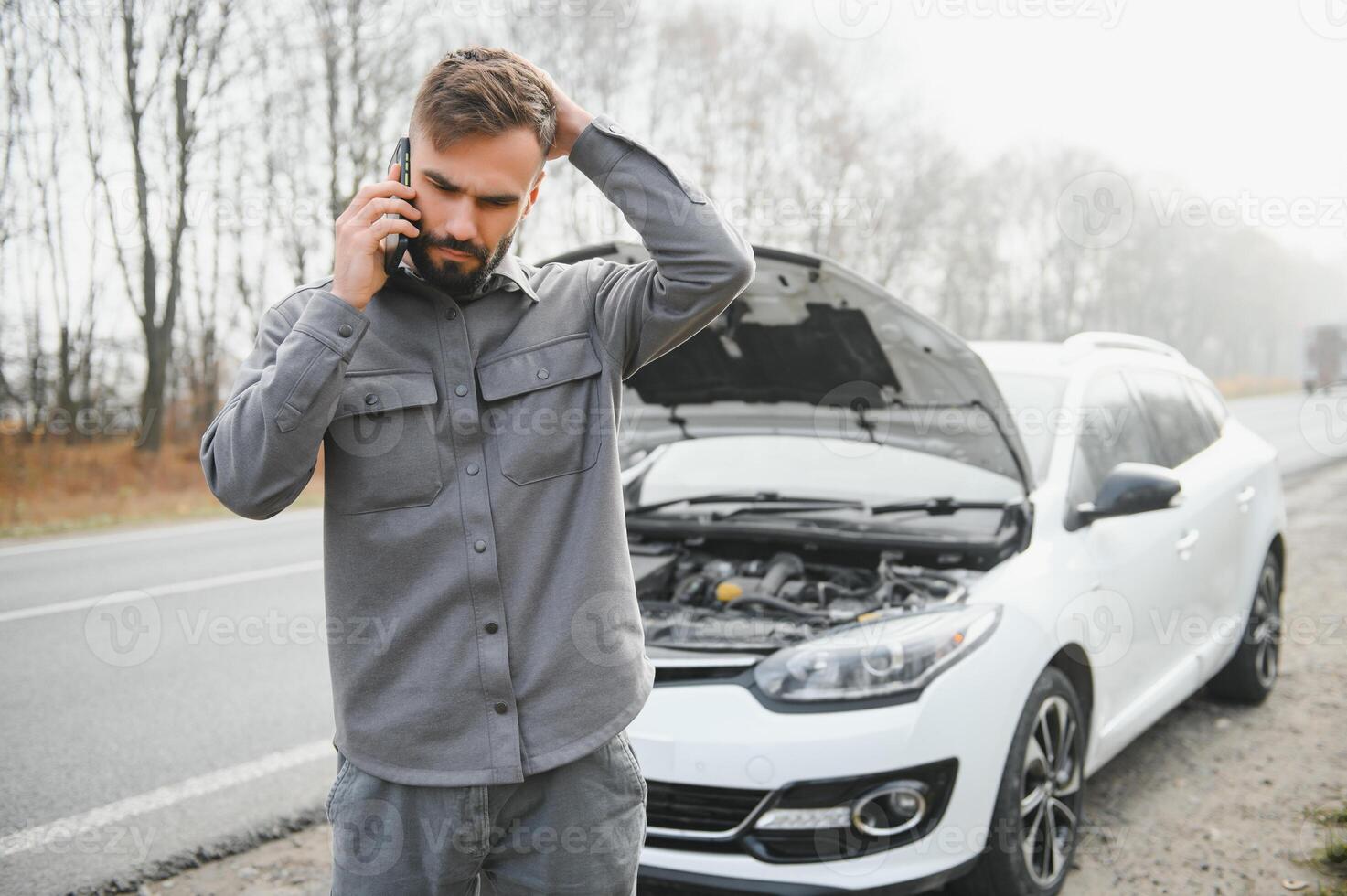 Sad driver holding his head having engine problem standing near broken car on the road. Car breakdown concept photo