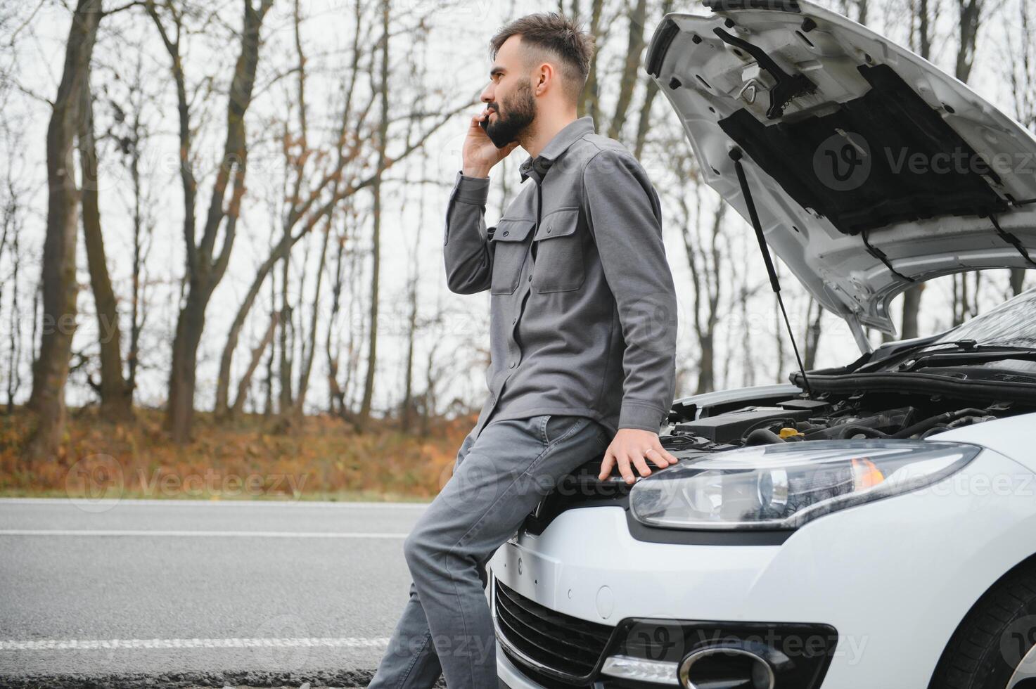 Sad driver calling car service, opening hood, having engine problem standing near broken car on the road. Car breakdown concept photo