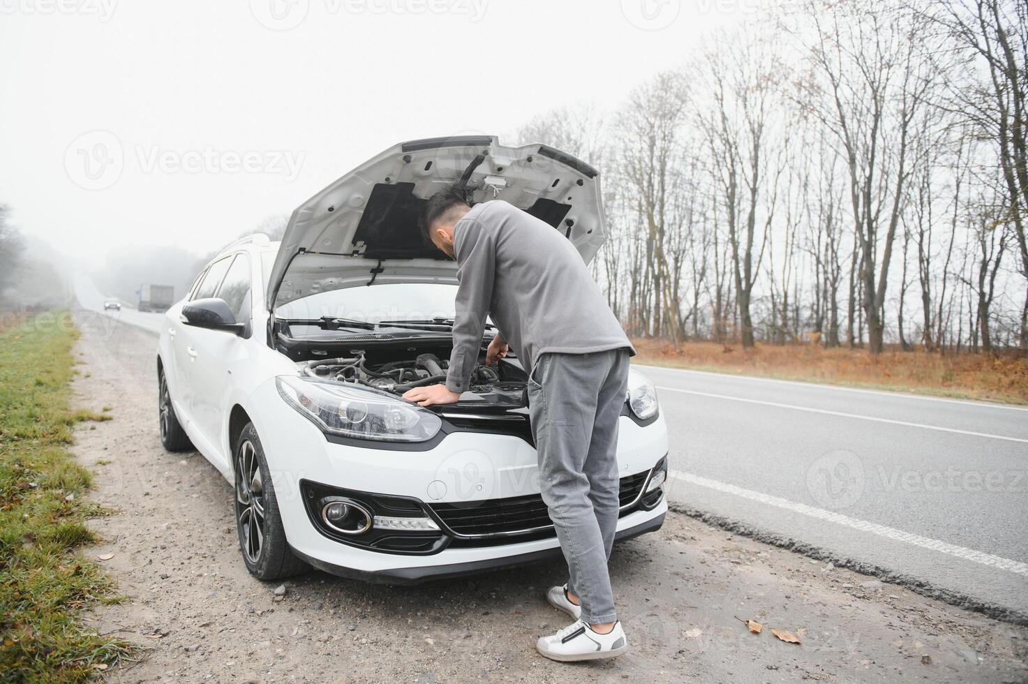 young stressed man having trouble with his broken car looking in frustration at failed engine photo