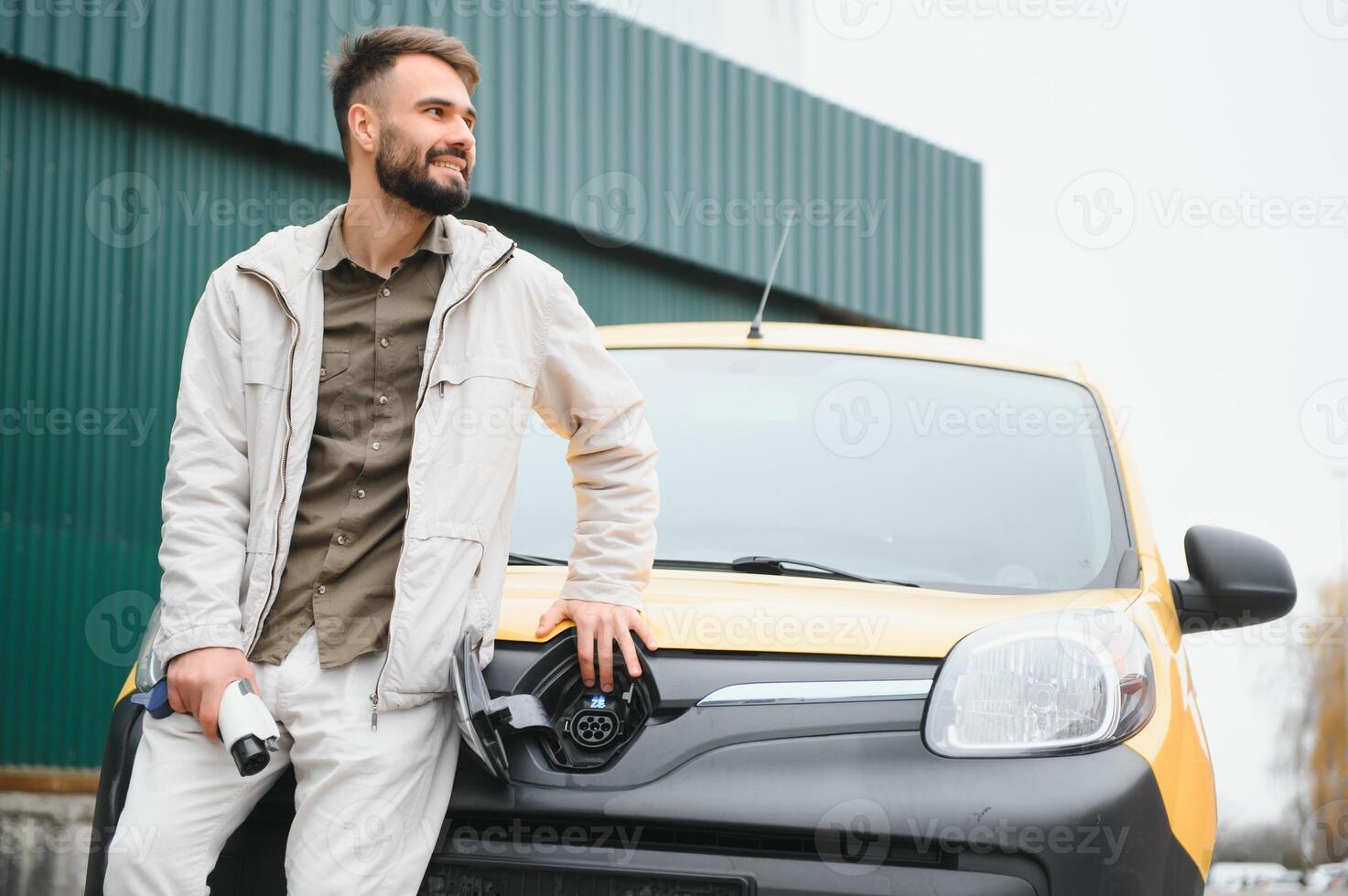 Portrait of a young man standing with charging cable near the charging station photo