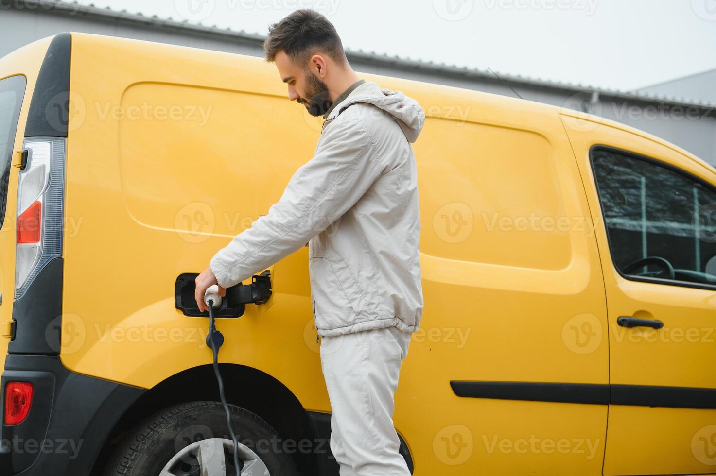 Man Holding Power Charging Cable For Electric Car In Outdoor Car Park. And he s going to connect the car to the charging station in the parking lot near the shopping center photo