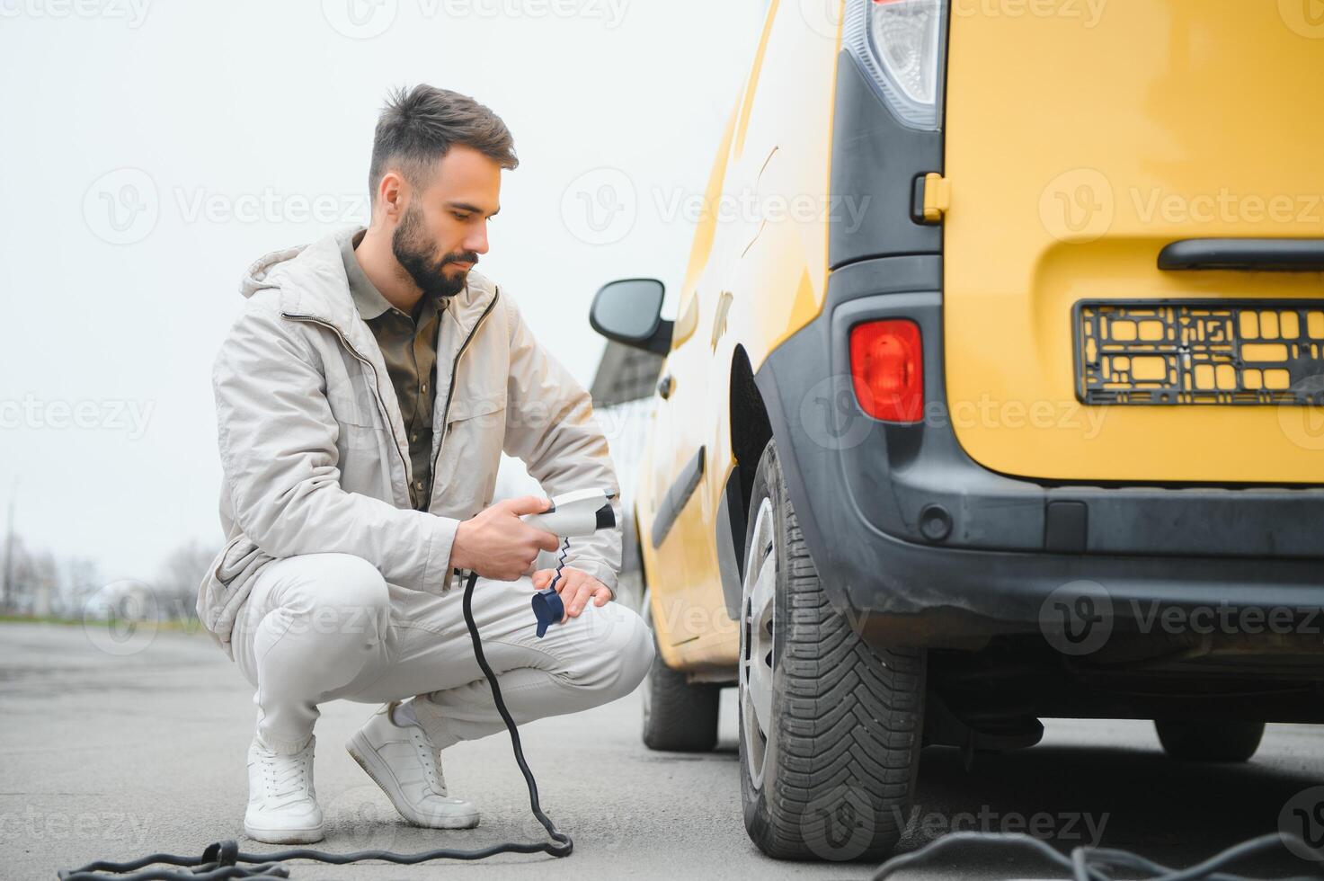 Man Holding Power Charging Cable For Electric Car In Outdoor Car Park. And he s going to connect the car to the charging station in the parking lot near the shopping center photo