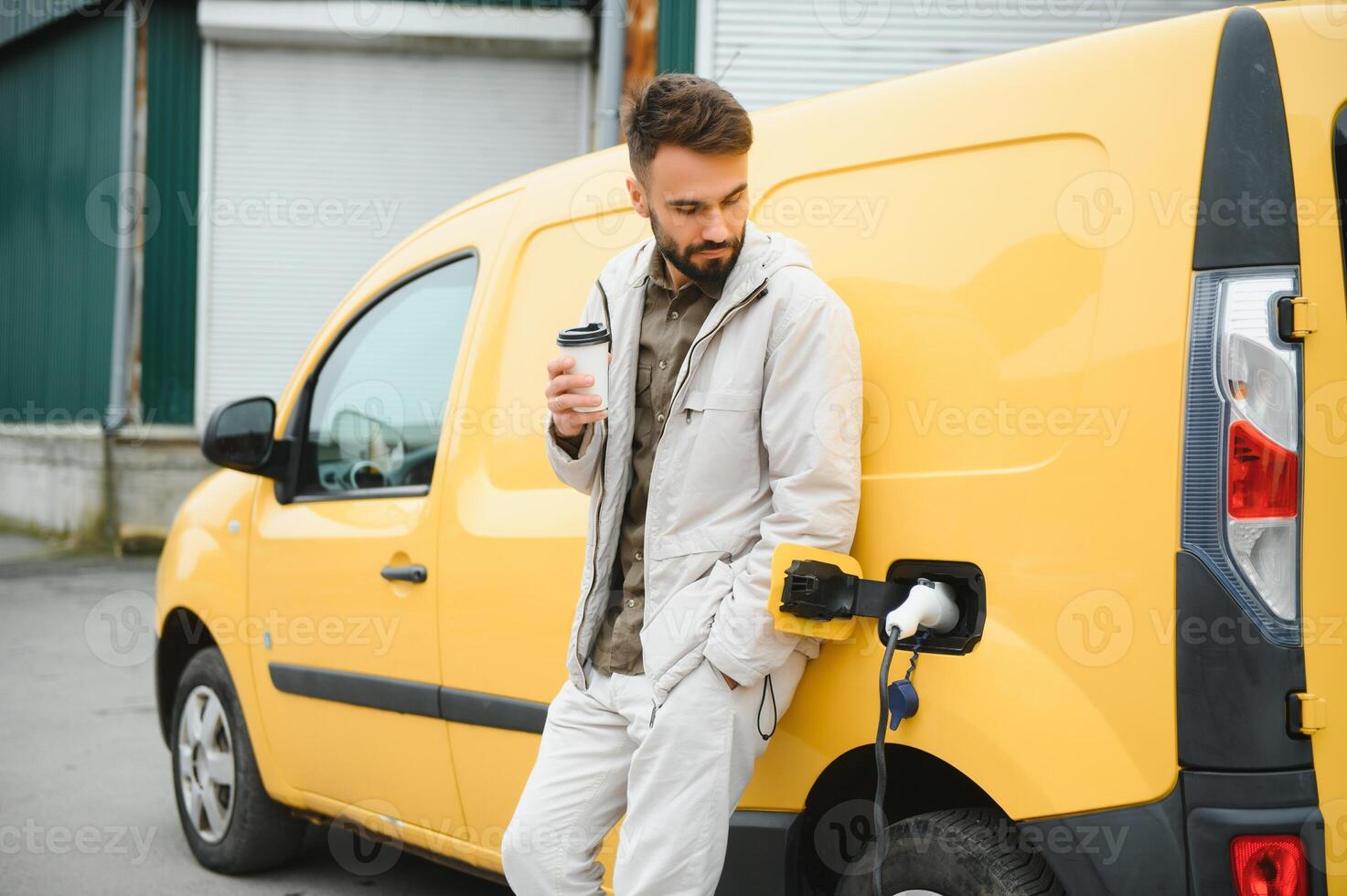 Handsome man drinking coffee while charging electric car photo