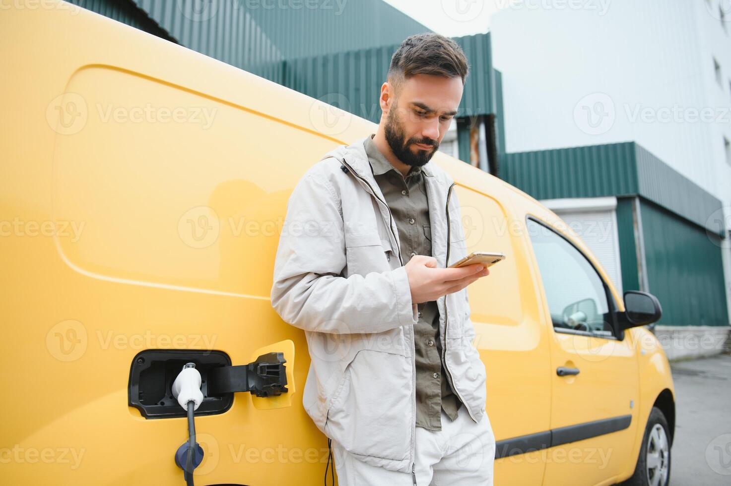 Portrait of a young man standing with charging cable near the charging station photo