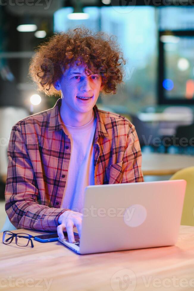 Portrait of Caucasian male freelancer in trendy apparel sitting at cafeteria table and doing remote work for programming design of public website, skilled software developer posing in coworking space. photo
